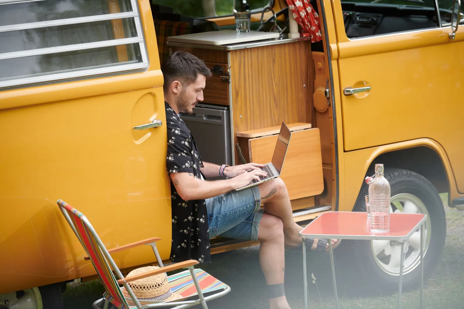 Junger Mann mit Laptop in einem gelben Camper