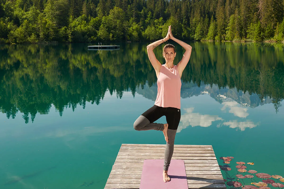 Frau macht Yoga auf einem Steg an einem wunderschönen Bergsee