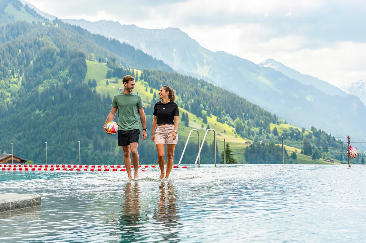 Mann und Frau gehen durchs untiefe Wasser eines Pools in einer Berglandschaft