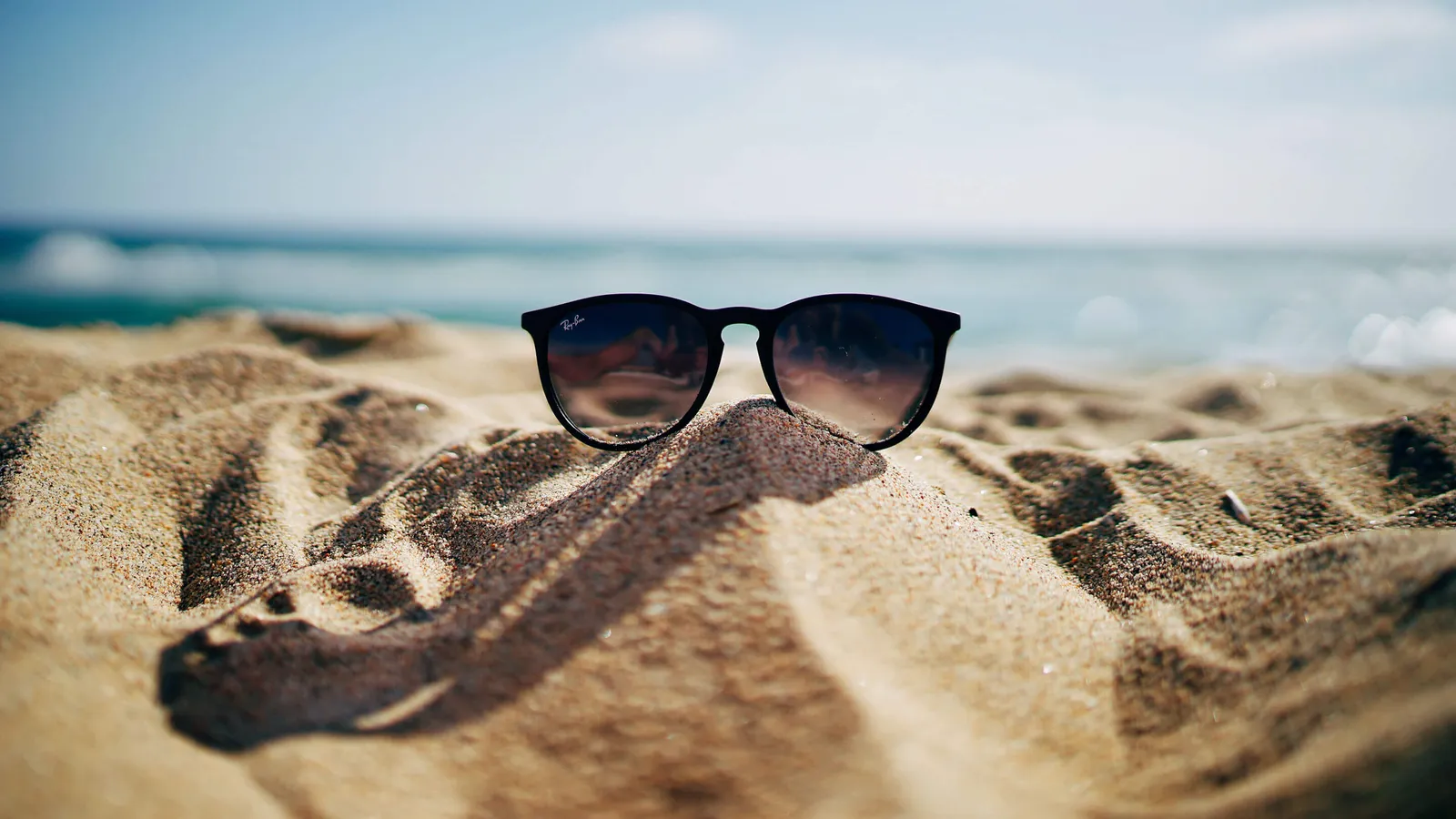 Sonnenbrille liegt am Strand auf dem Sand, im Hintergrund das Meer