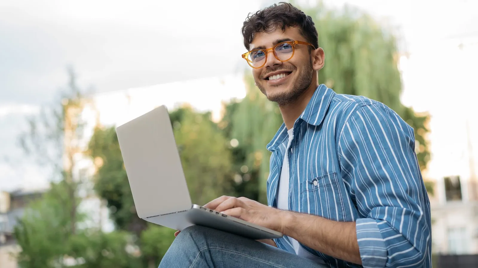 Junger Mann mit Laptop sitzt draussen und arbeitet am Laptop