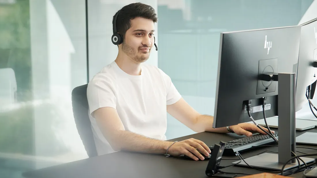 Ein Mann sitzt am Computer und hat ein Headset auf dem Kopf