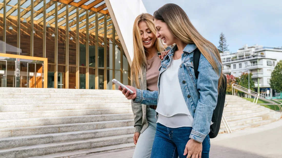 Zwei junge Frauen schauen lachend aufs Smartphone