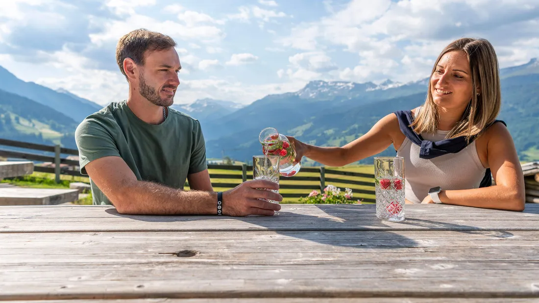 Zwei Personen sitzen draussen an einem Picknicktisch und giessen Wasser mit Beeren ein