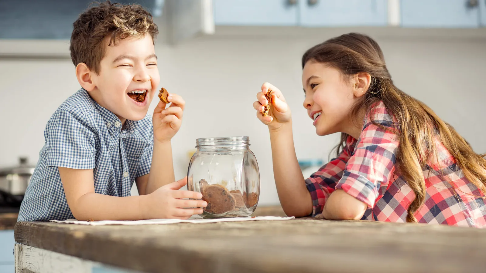 Zwei Kinder essen Kekse aus einer Dose und lachen dabei