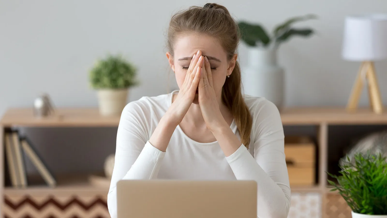 Frau sitzt mit Händen vor dem Gesicht am Laptop