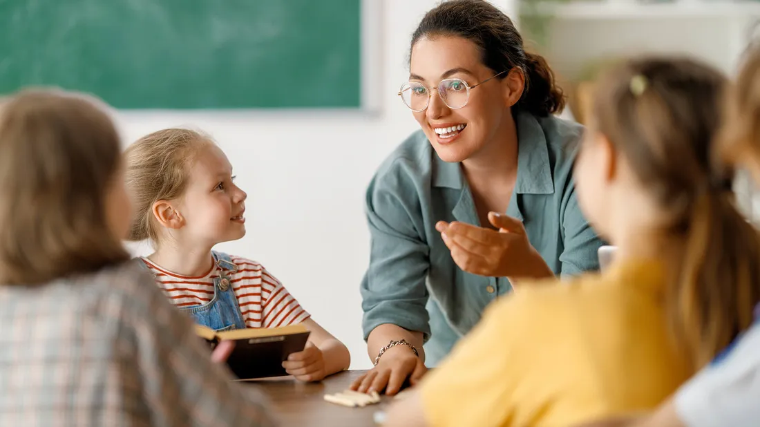 Lehrerin erklärt ihren Schüler*innen etwas am Tisch