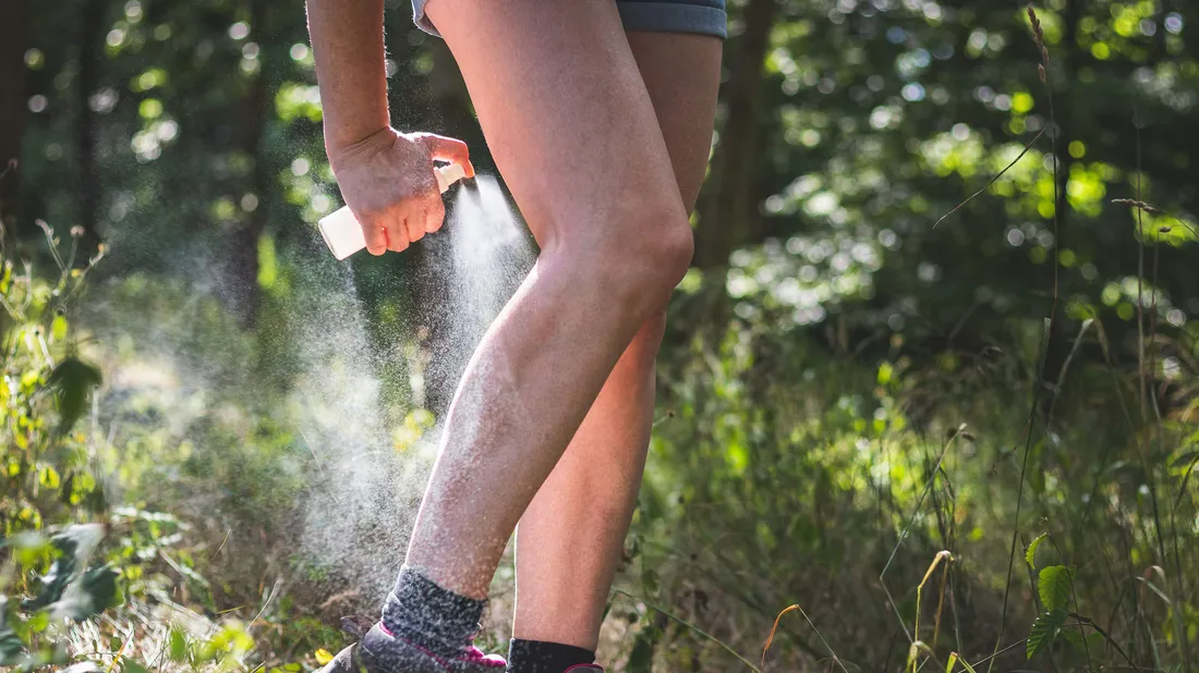 Person sprüht sich Insektenspray auf die Beine