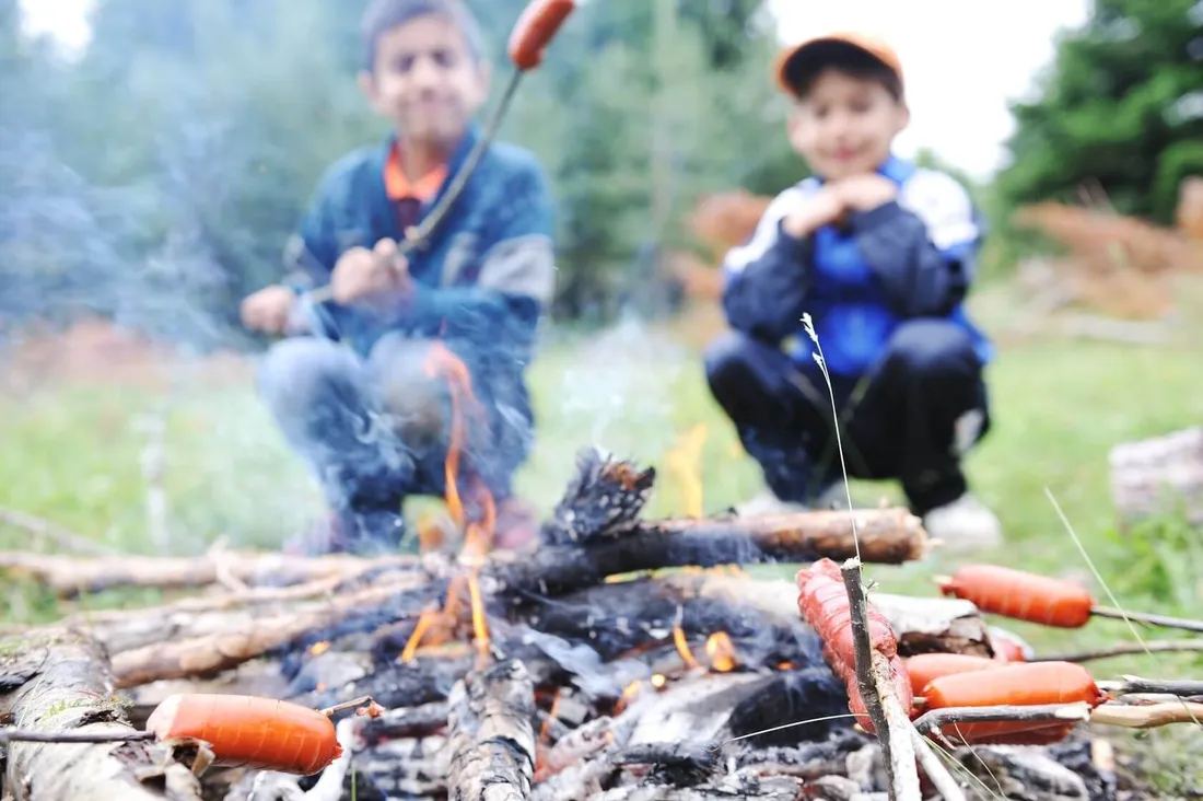 Zwei Kinder halten Cervelats übers Feuer