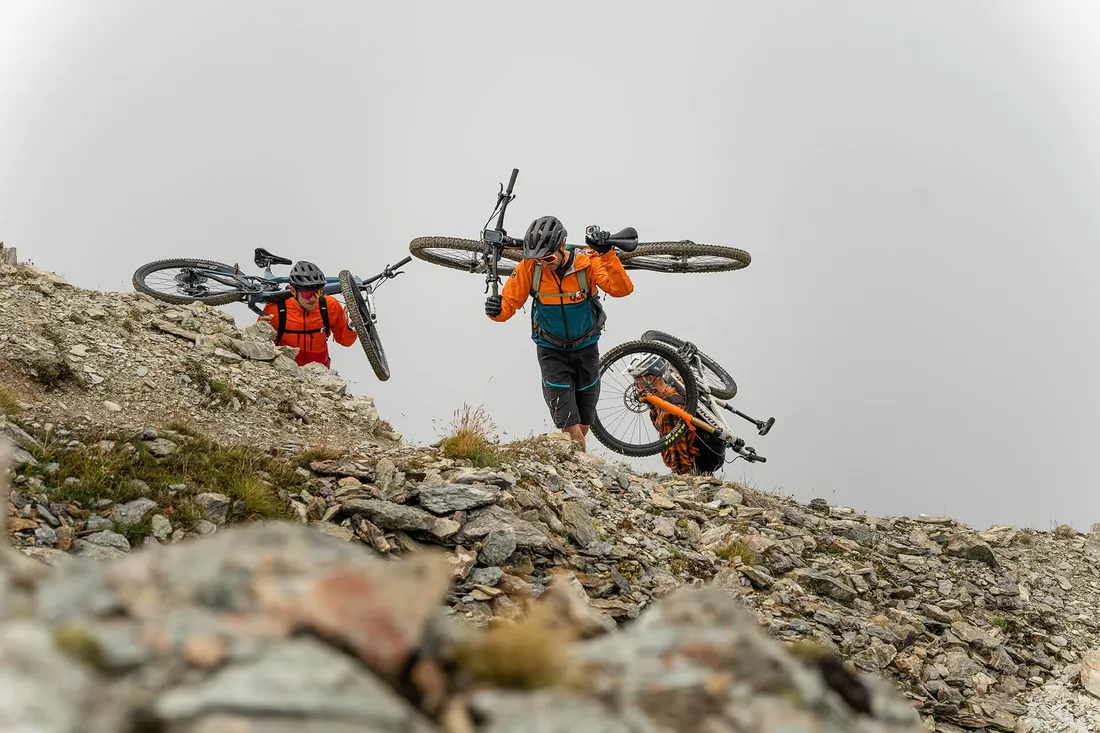 Drei Mountainbiker tragen ihr Bike einen steilen Weg hinauf