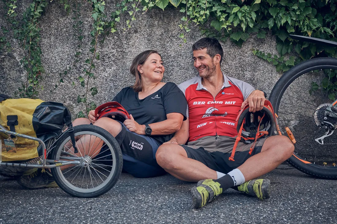 Zwei Radfahrer machen an eine Wand gelehnt eine Pause